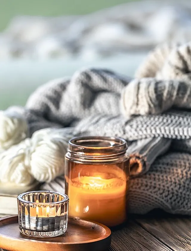 Warm, inviting scene with lit candles, cozy knit blankets, and soft textures.