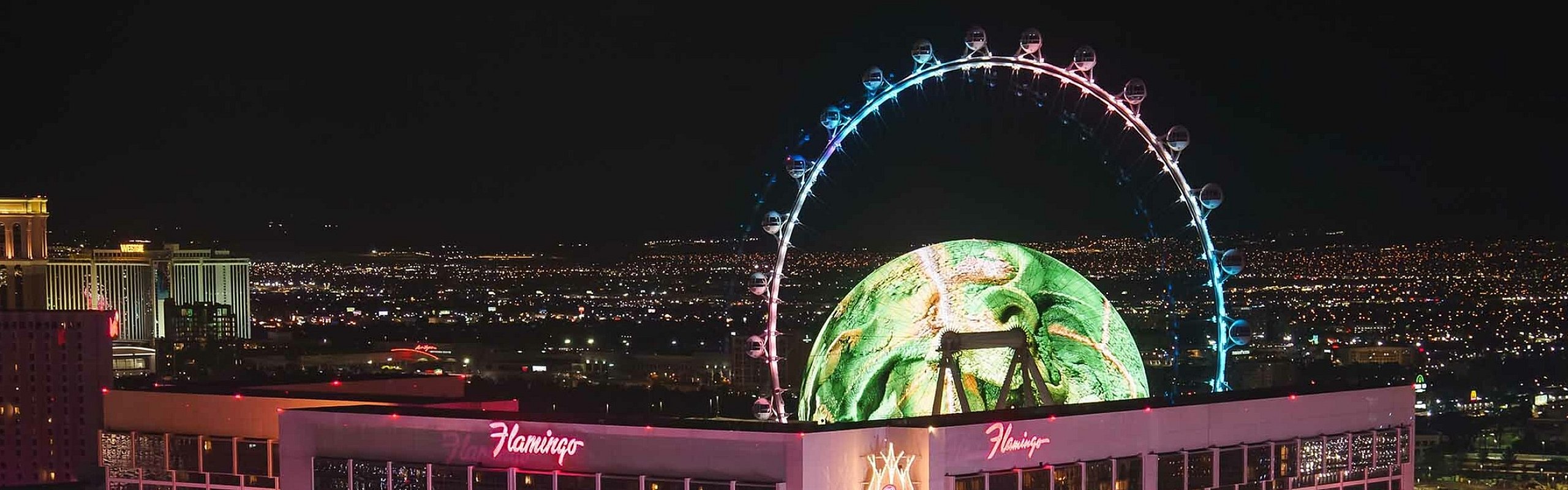 Brightly lit hotel at night with a stunning observation wheel against a cityscape backdrop.