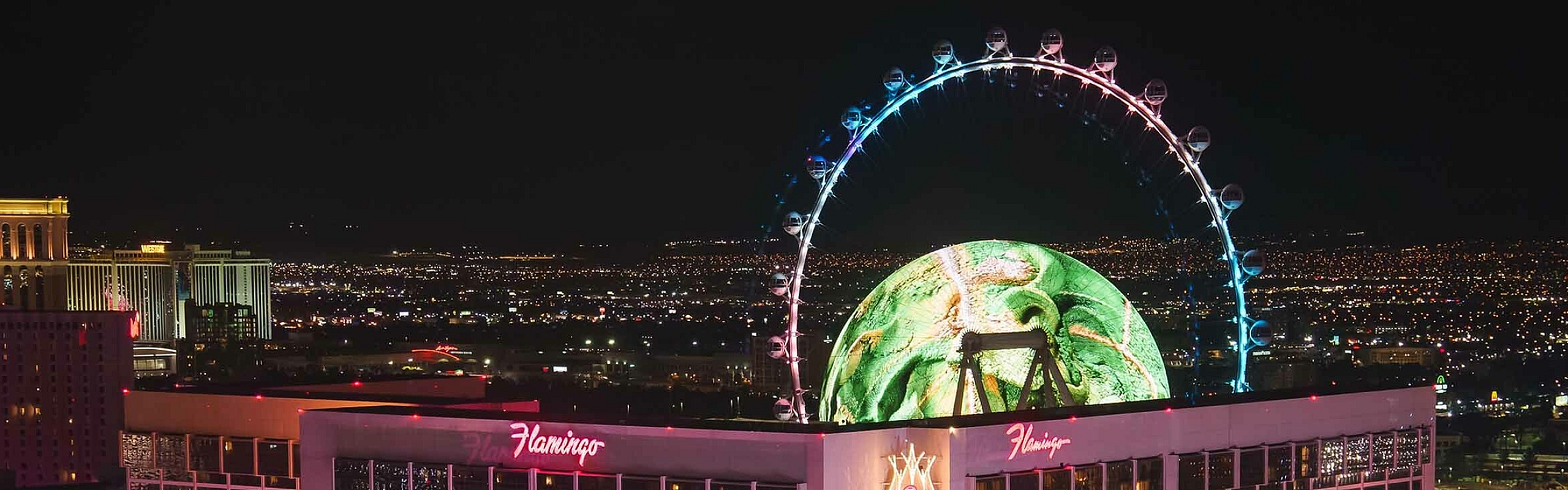 Dazzling evening view of a luxurious hotel with bright neon lights and a Ferris wheel in the backdrop.