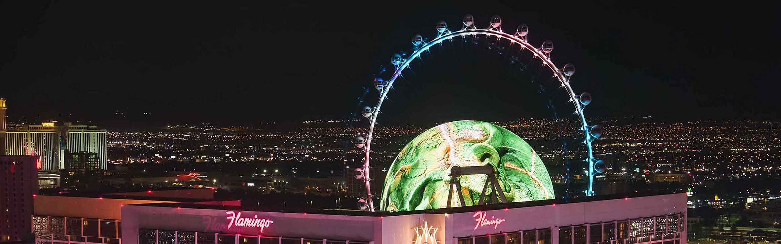 Stunning night view of a brightly lit hotel with a giant observation wheel in the background.