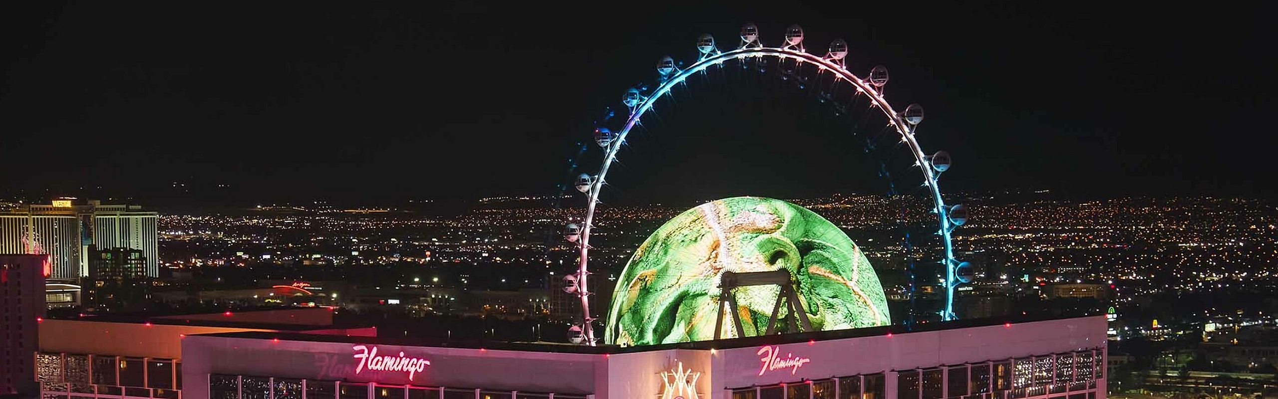 Illuminated hotel building with a large observation wheel at night, offering stunning city views.