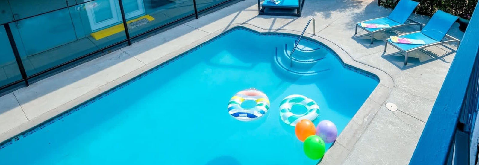 Inviting swimming pool with vibrant float rings and sun loungers under a clear sky.