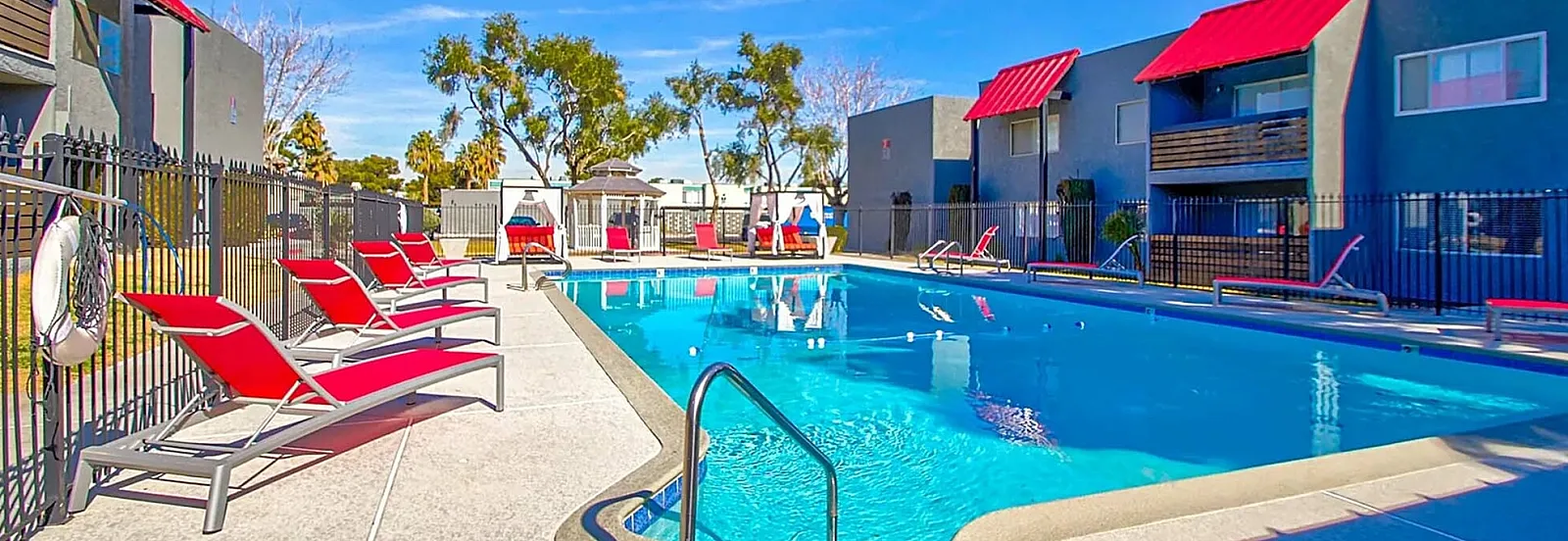 Chic apartment complex with vibrant red accents and luxurious swimming pool surrounded by stylish lounge chairs.