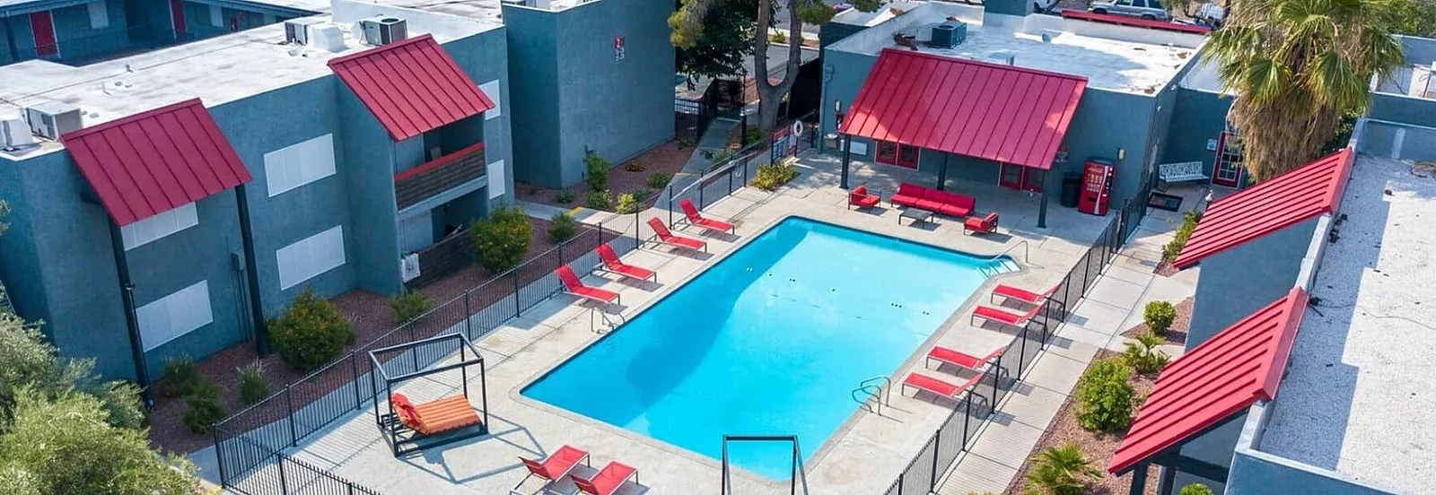 Aerial view of a vibrant apartment complex with a central pool, surrounded by lush greenery and modern architecture.