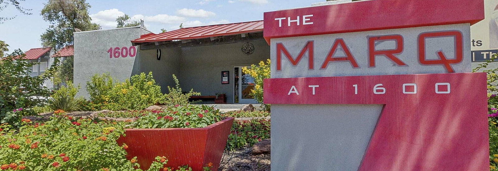 Vibrant garden and modern signage at The MARQ at 1600, showcasing a welcoming entrance.