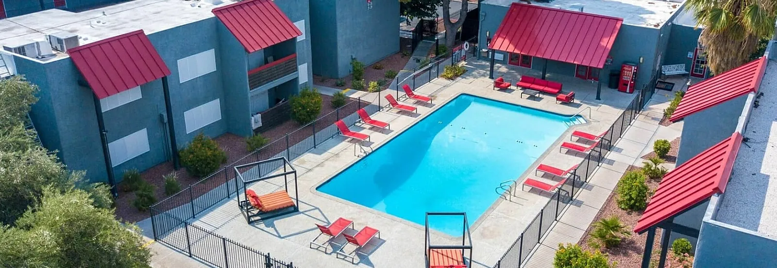 Aerial view of a modern apartment complex featuring a central pool area with red-accented buildings.