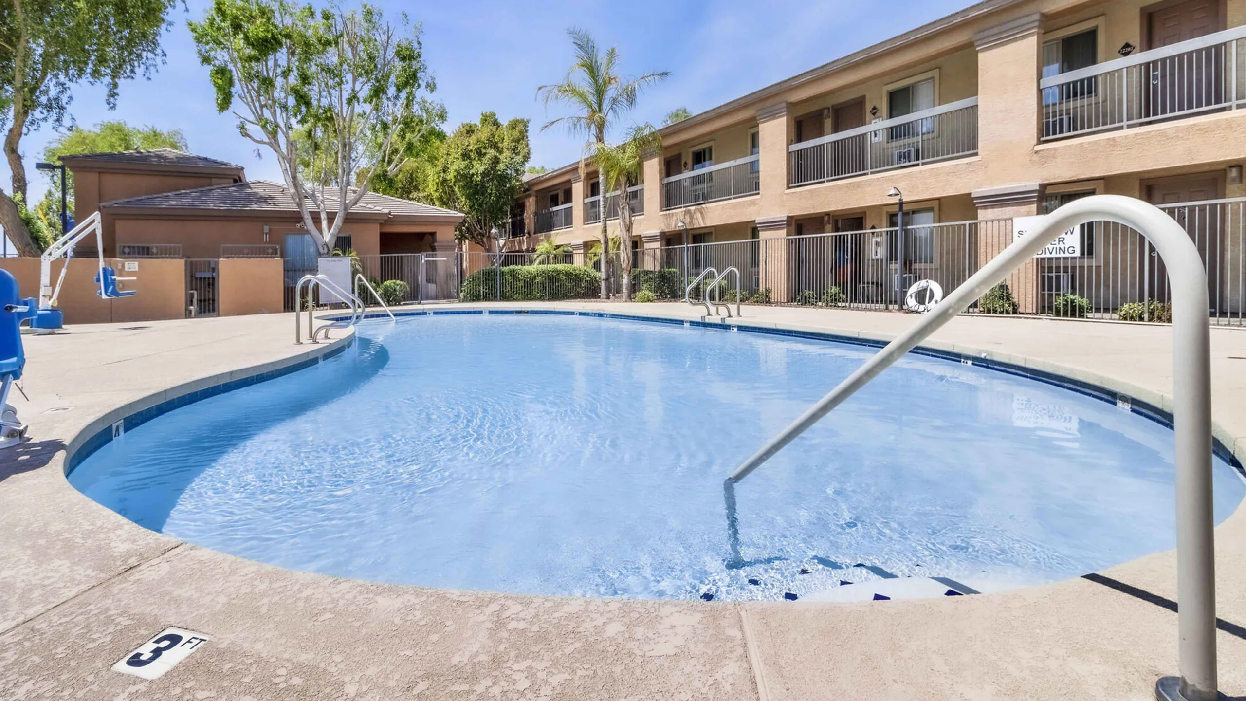Inviting outdoor pool area with sparkling blue water, surrounded by elegant apartment units, lush greenery, and ample lounge space for relaxation.
