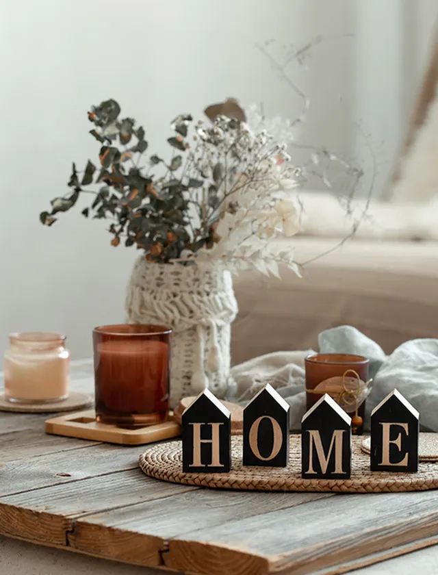 Cozy living space with a rustic wooden table, elegant candles, decorative vase, and home-themed decor blocks.