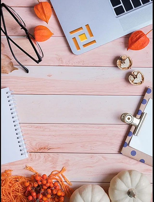 Chic autumn-themed desk setup with laptop, glasses, notebook, and decorative pumpkins on a stylish wooden surface.