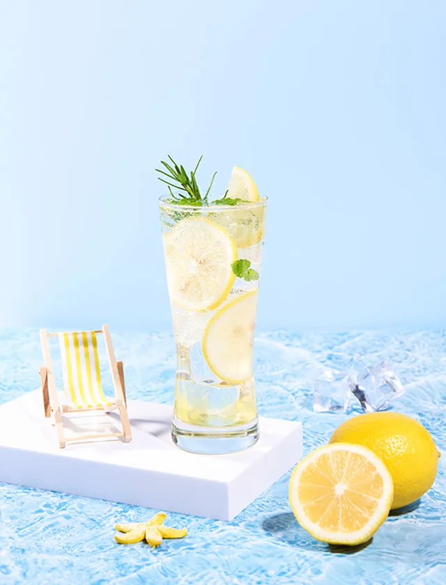 Refreshing summer lemonade with fresh lemon slices and mint, served in a tall glass, evoking a beachside vibe with a mini deck chair and vibrant blue background.
