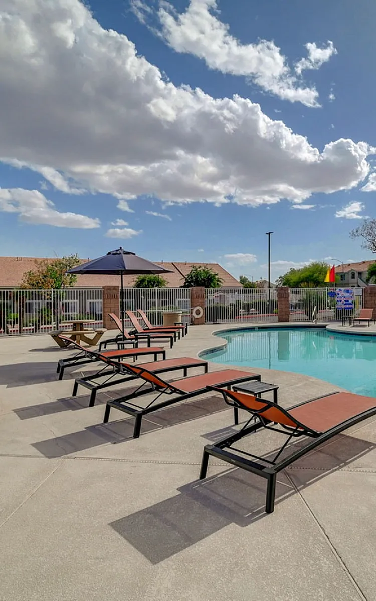 Inviting outdoor pool area with comfortable lounge chairs, surrounded by lush greenery and a bright, sunny sky.