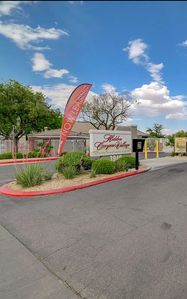 Inviting entrance of Hidden Canyon Village with vibrant flags, lush greenery, and a welcoming atmosphere.