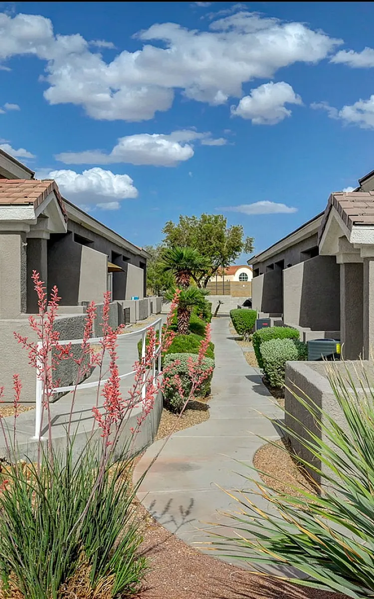 Charming apartment complex with modern architecture, featuring a beautifully landscaped walkway under a vibrant blue sky.