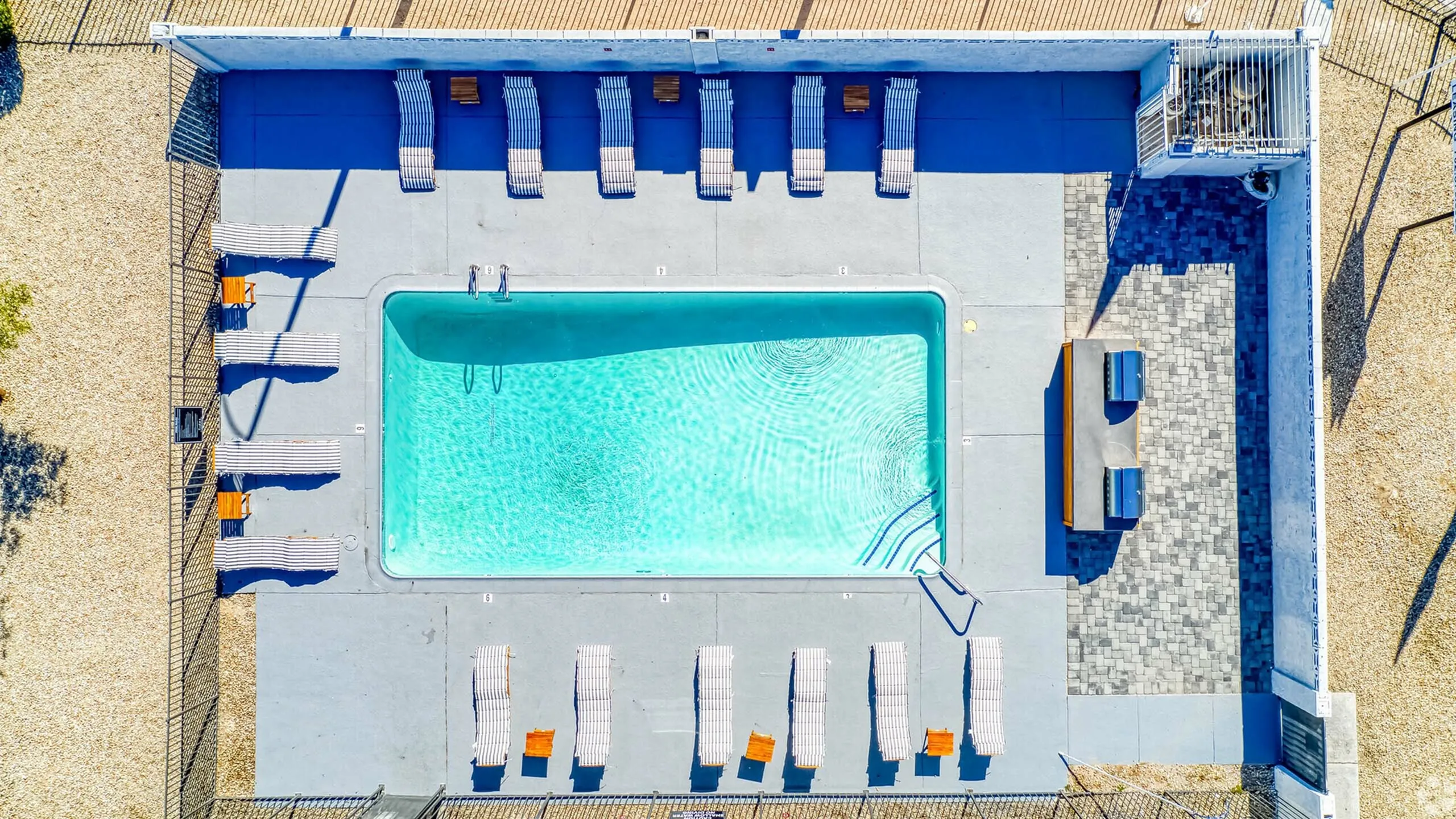 Inviting aerial view of a private swimming pool surrounded by sun loungers and a shaded seating area, perfect for relaxing and entertaining.