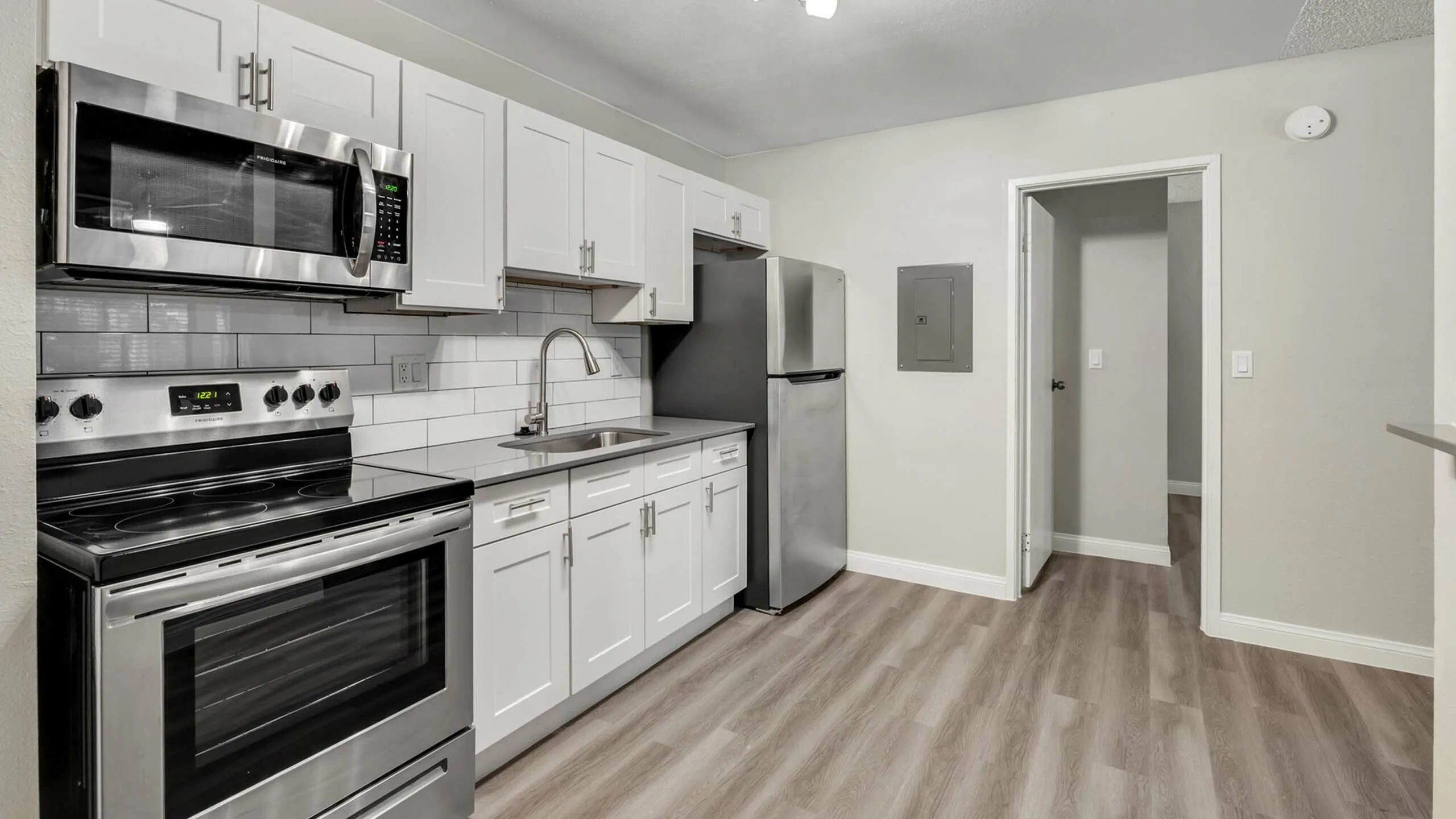 Modern kitchen with sleek stainless steel appliances, elegant white cabinetry, and stylish wood flooring, offering a sophisticated cooking space.