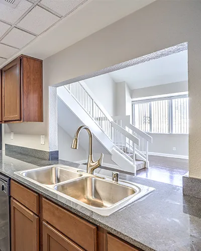 Bright and airy kitchen with modern sink overlooking a sunlit living room and staircase, featuring elegant countertops and warm cabinetry.