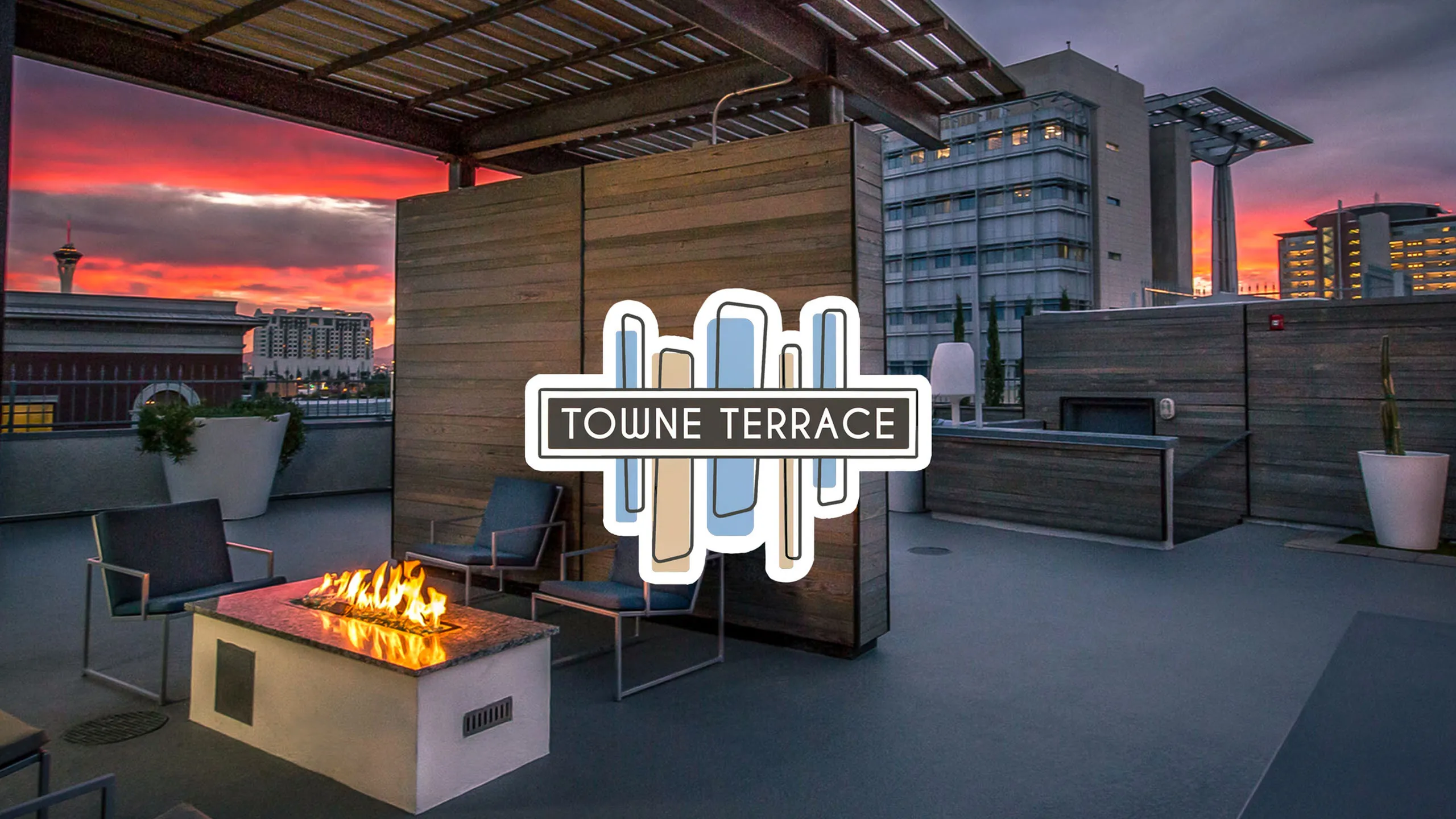 Chic rooftop terrace at Towne Terrace with cozy fire pit seating under a vibrant sunset skyline.