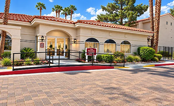 Charming leasing office of Villa Monterey with elegant Mediterranean architecture, lush landscaping, and palm trees under a bright blue sky.