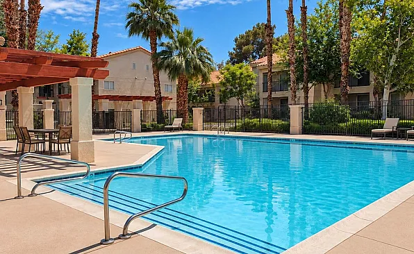 Luxurious apartment complex pool area featuring sparkling blue waters, surrounded by lush palm trees and elegant loungers for ultimate relaxation.