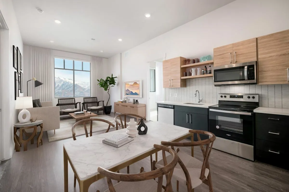 View of Park Avenue's 1-Bedroom Model Showing Mountain Views, Couch, Dining Room Table, Stainless Steel Kitchen Appliances, and Wood Cabinetry