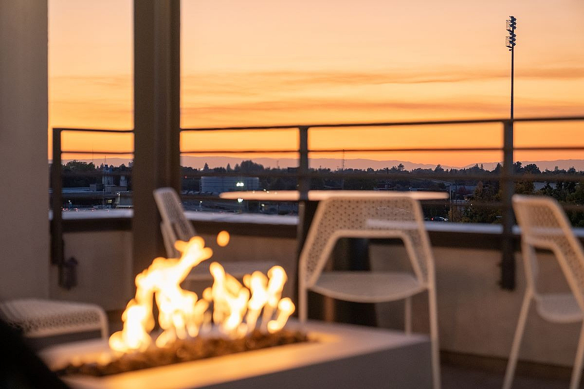 Inviting rooftop patio with modern seating and a warm fire pit overlooking a stunning sunset.