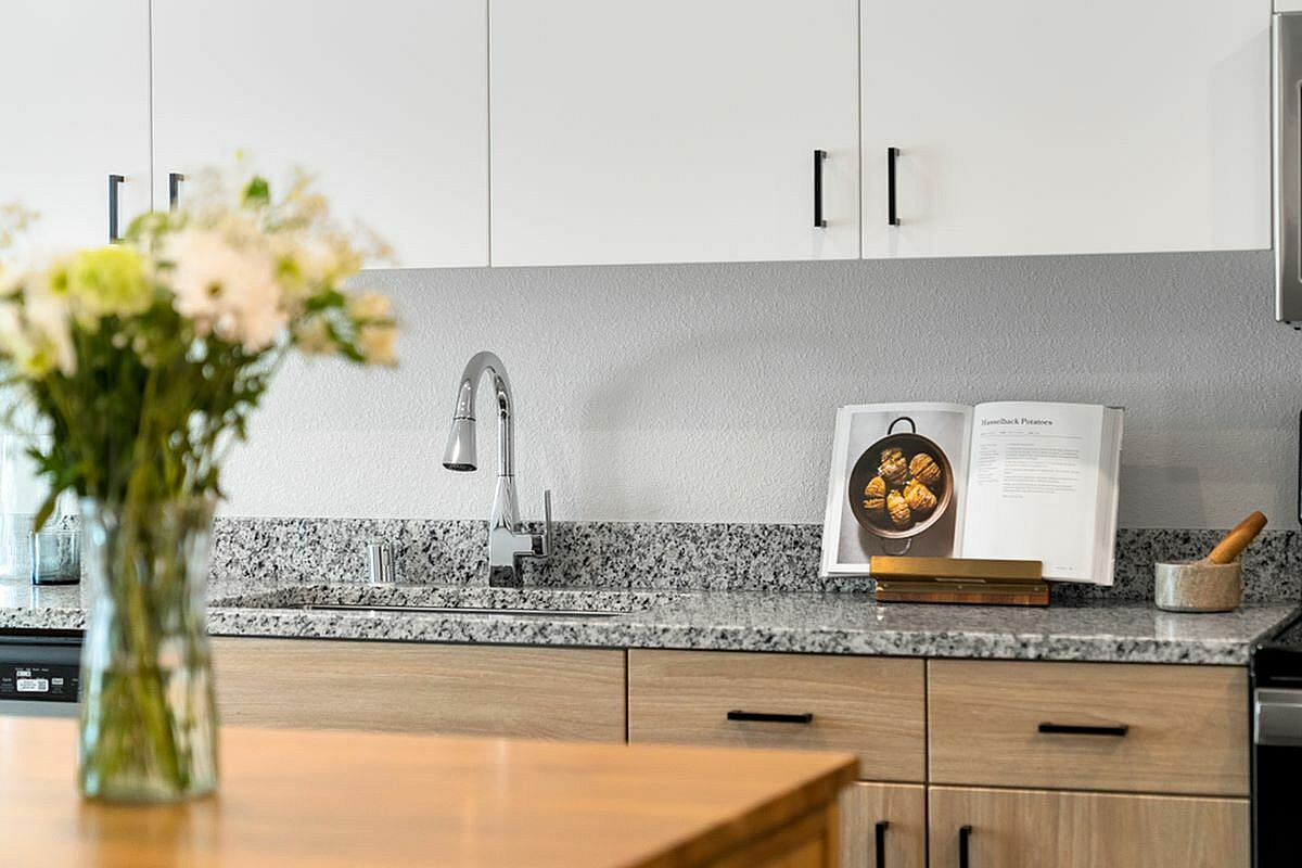 Modern kitchen countertop with sleek granite, wooden cabinets, and a vase of flowers.