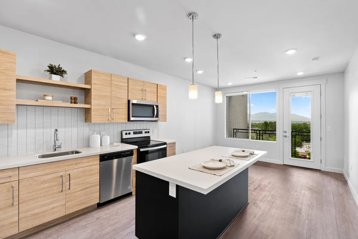 Modern kitchen with sleek wooden cabinets, stainless steel appliances, and a spacious island, complemented by natural light from the large window and balcony view.