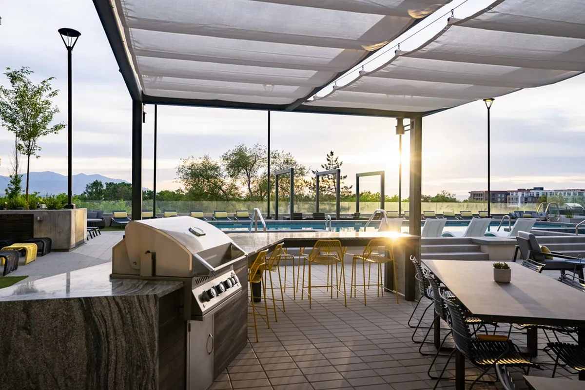 Inviting outdoor patio with modern grill, sleek seating, and serene poolside view at sunset.