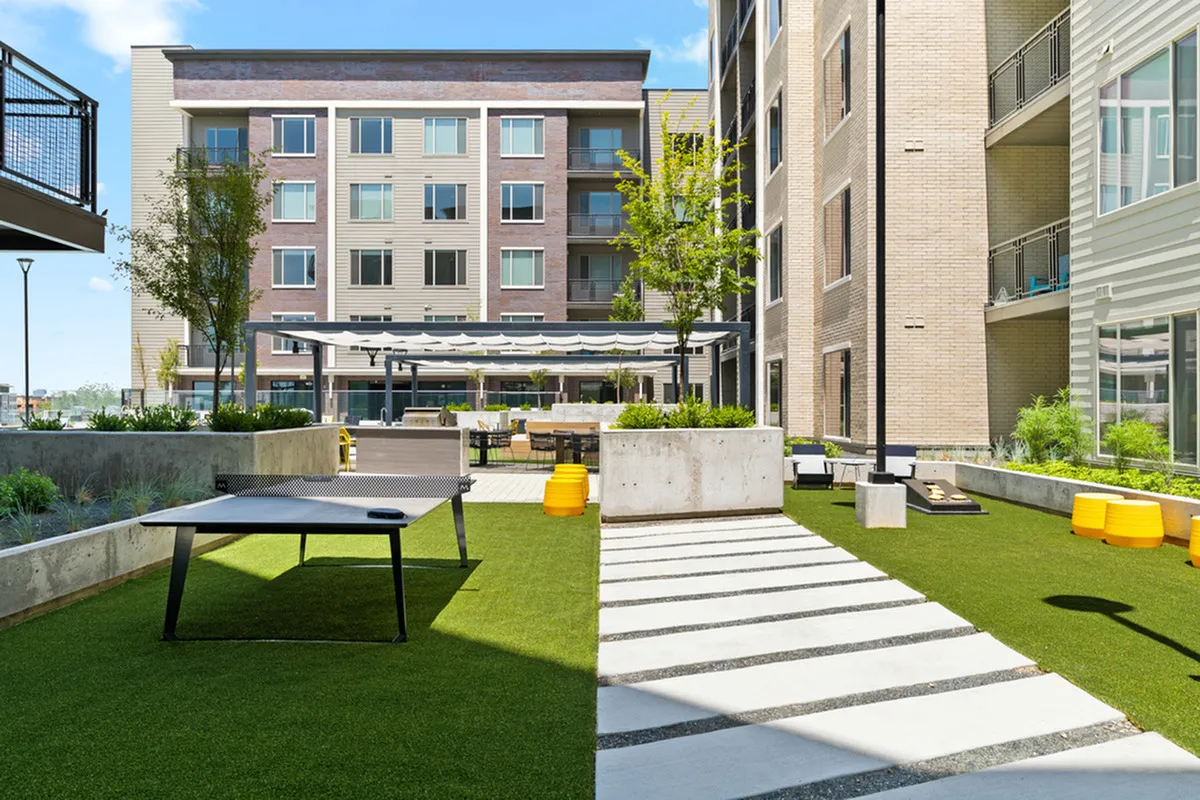 Modern apartment complex courtyard featuring lush green spaces, a ping pong table, and stylish outdoor seating for relaxation and socializing.