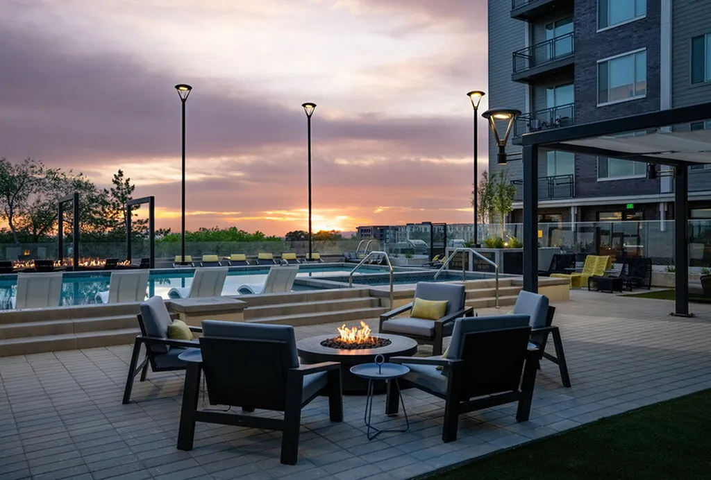 Luxurious apartment patio with a cozy fire pit, stylish seating, and a serene pool under a breathtaking sunset sky.