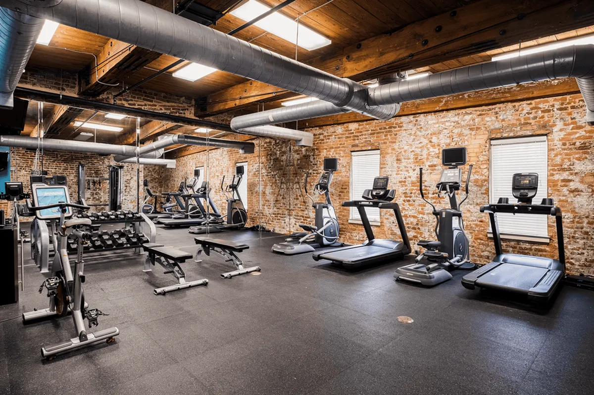 Modern gym at Alpha Mill Apartments featuring exposed brick walls, premium treadmills, and a versatile weight training area.