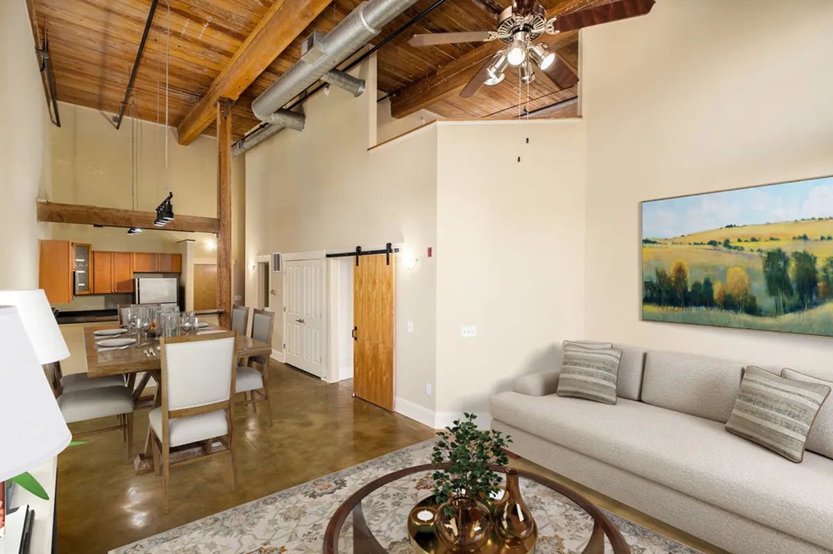 Modern loft-style apartment with exposed wood beams, industrial ceiling, and elegant dining space connected to an open kitchen. Alpha Mill Apartment's cozy living area featuring a plush sofa and large scenic artwork.