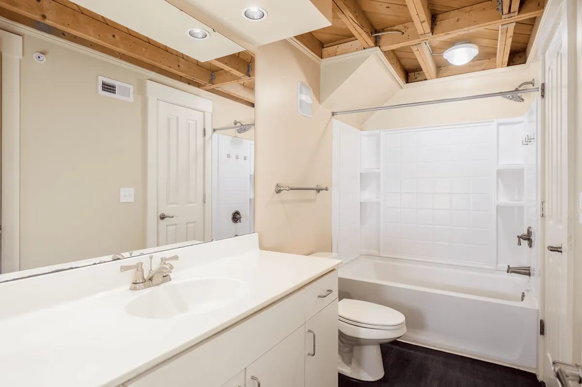 Elegant bathroom in Alpha Mill Apartments featuring a luxurious white bathtub, sleek vanity, and rustic exposed wood ceiling beams.