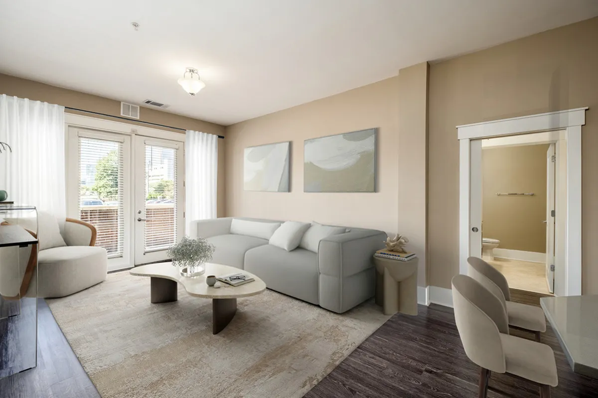 Bright, inviting living room at Alpha Mill Apartments with a modern gray sofa, elegant decor, and natural light streaming through large French doors.