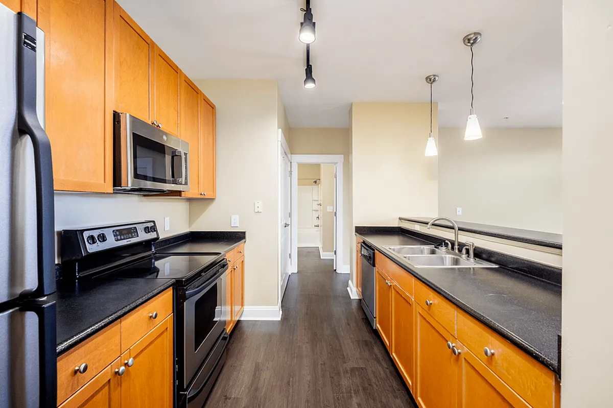 Alpha Mill Apartment's modern kitchen with sleek black countertops, stainless steel appliances, and warm wooden cabinets under stylish pendant lighting.