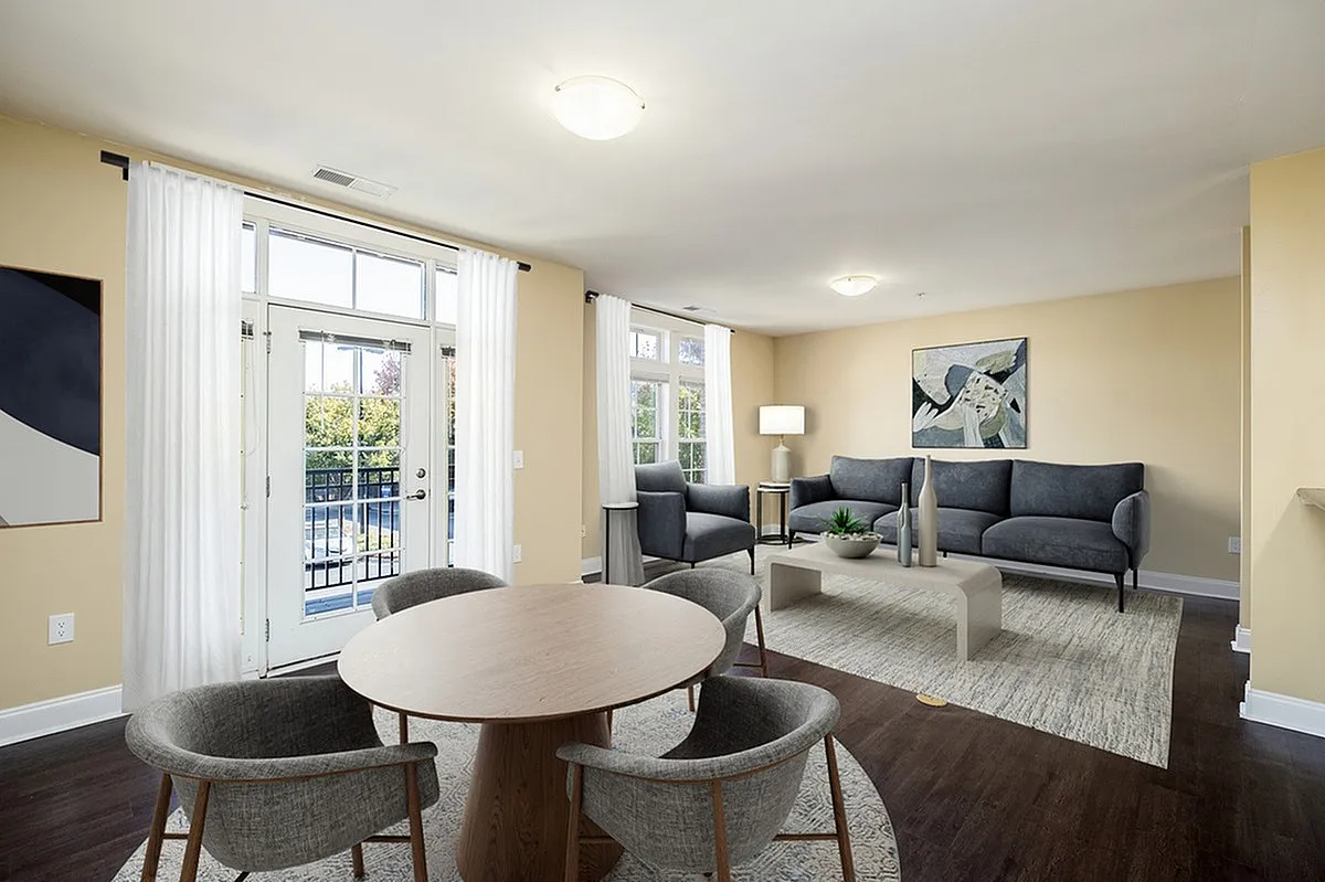 Elegant living room at Alpha Mill Apartments with modern gray furniture, stylish artwork, and abundant natural light through French doors.
