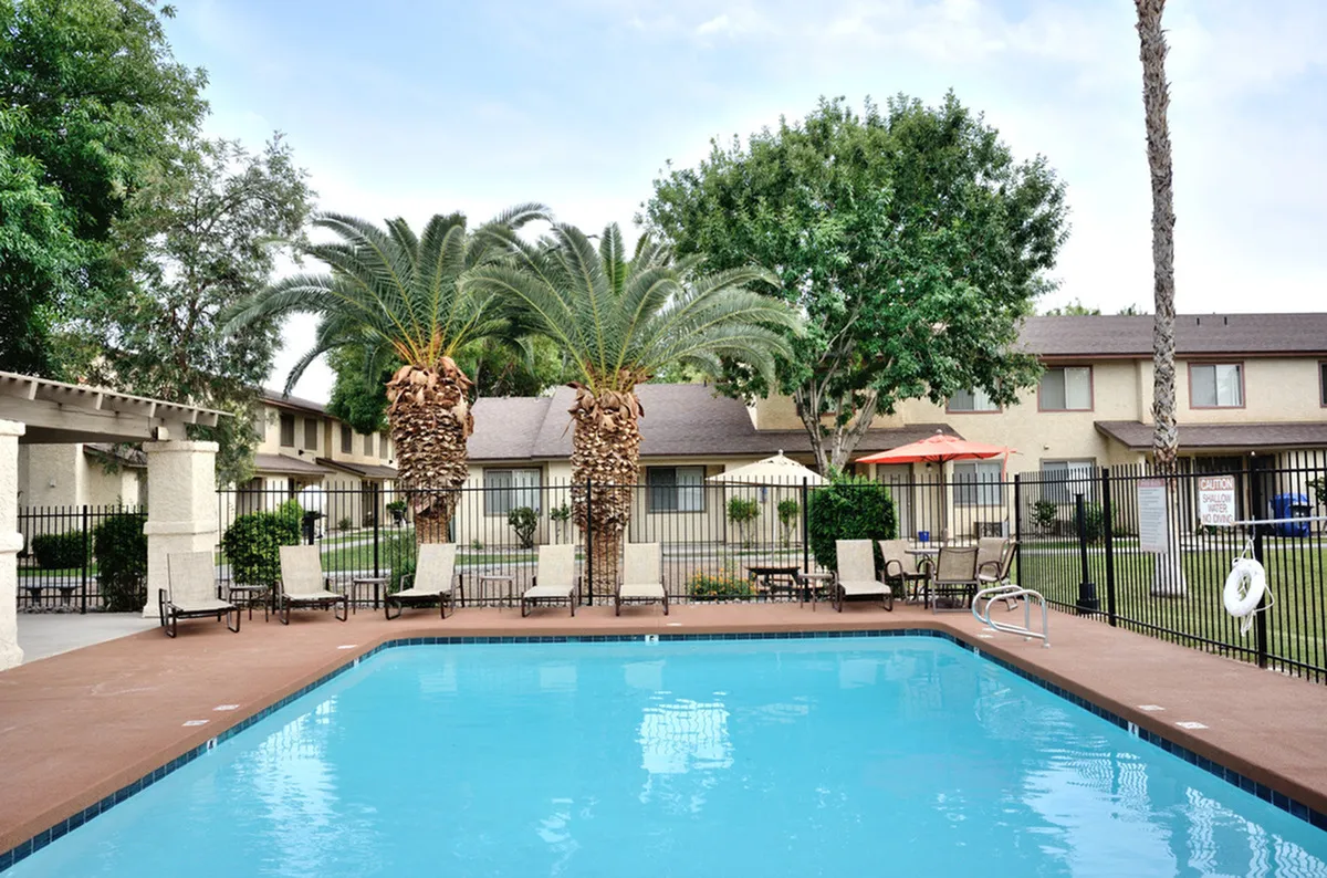 Camelot Apartment's inviting outdoor pool area with lush palm trees and comfortable lounge chairs, perfect for relaxation in a serene neighborhood setting.