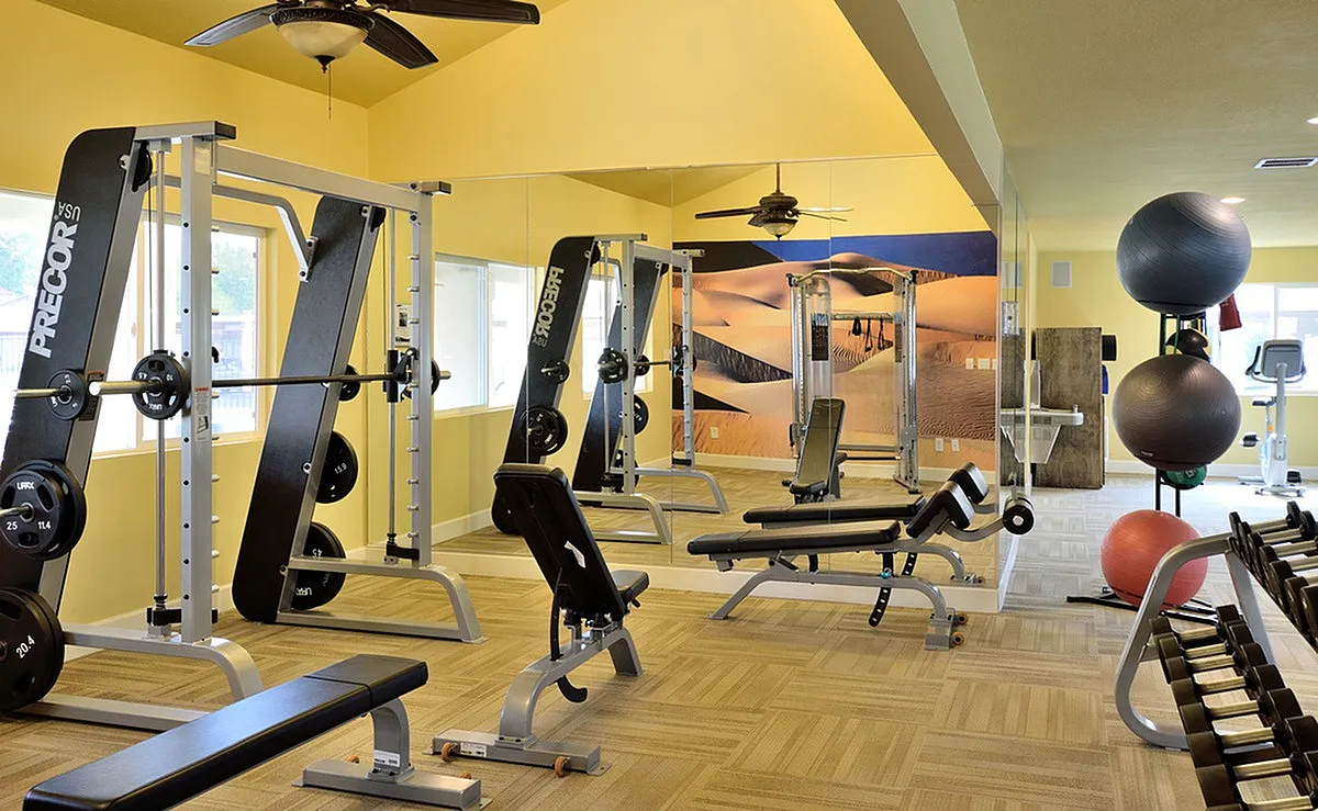 Camelot's modern fitness center with state-of-the-art equipment, vibrant yellow walls, and large mirrors enhancing the spacious feel.