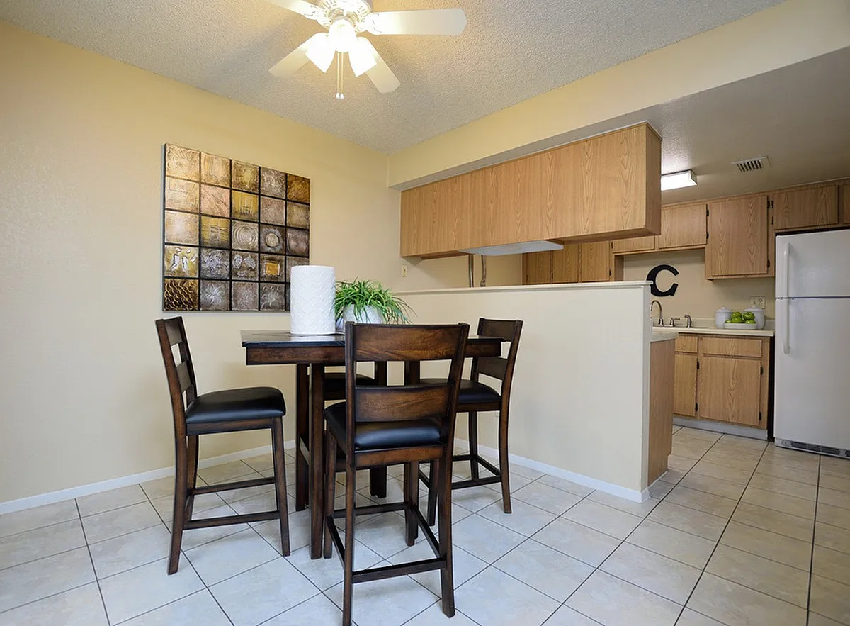 Bright dining area at Camelot Apartments in Yuma with elegant dark wood table and chairs, adjacent to a cozy open kitchen featuring wood cabinetry and modern appliances.