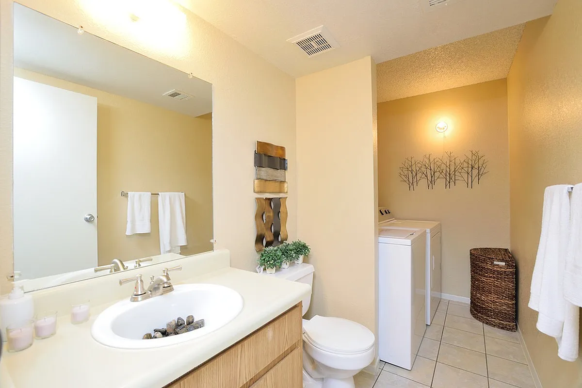 Bright Camelot Apartment's bathroom featuring a large mirror, decorative wall art, and a convenient laundry area with washer and dryer.