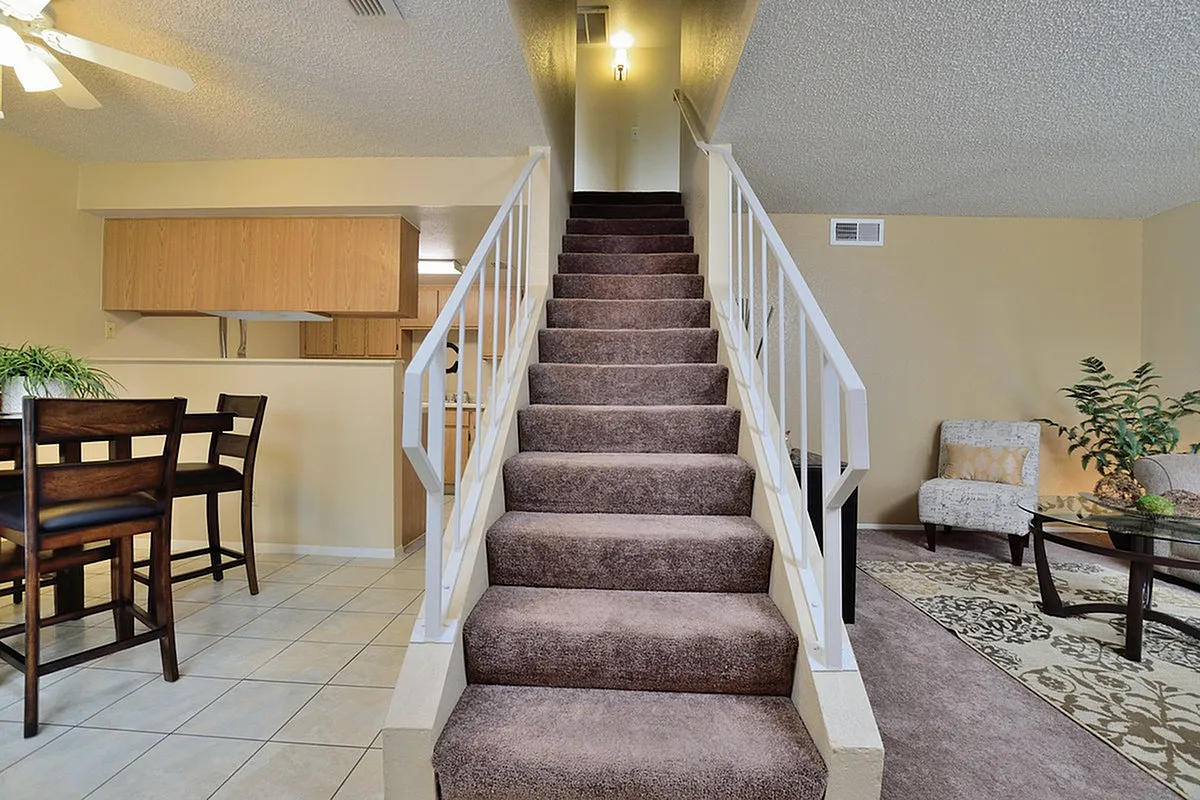 Inviting apartment interior with a stylish staircase leading to an upper floor, featuring an open-plan living space with modern dining area and cozy seating at Camelot Apartments in Yuma, Arizona.