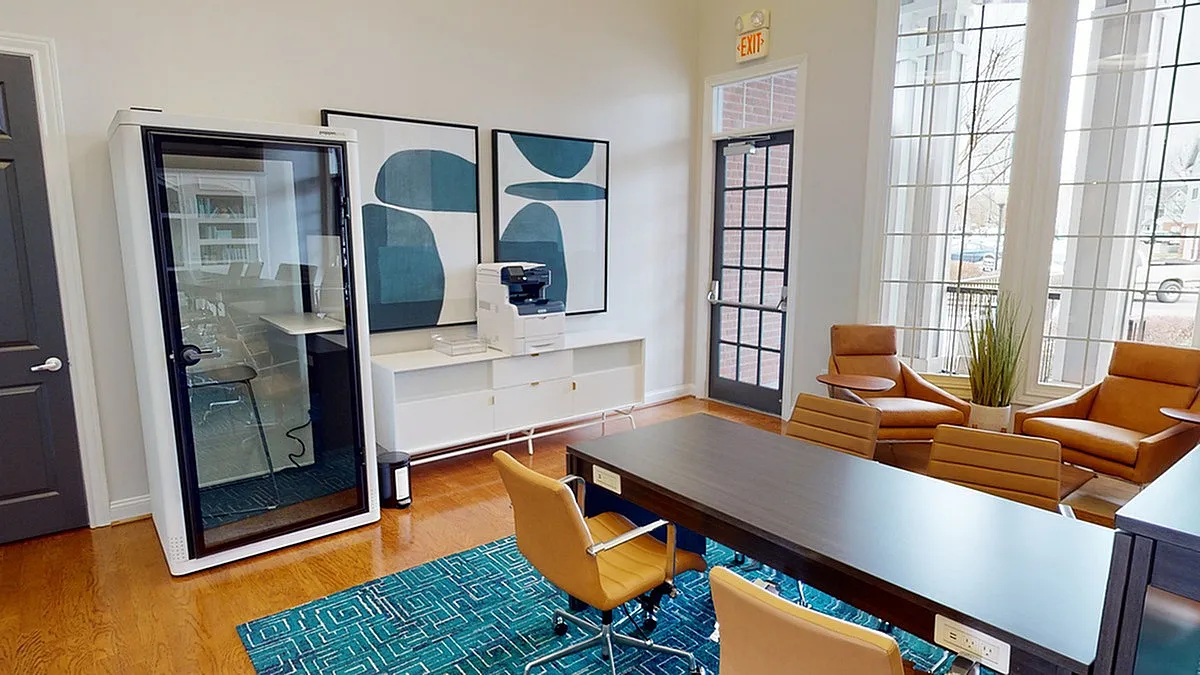 Apt CoWork coworking space at Cason Estates Apartments with modern furnishings, featuring a sleek conference pod, stylish chairs, and large windows for abundant natural light.
