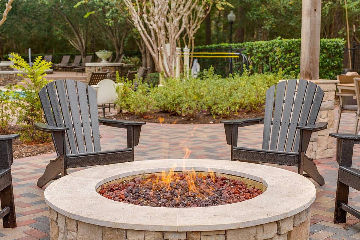 Inviting outdoor fire pit area with cozy Adirondack chairs, perfect for relaxing evenings at Raveneaux Apartments in North Houston.