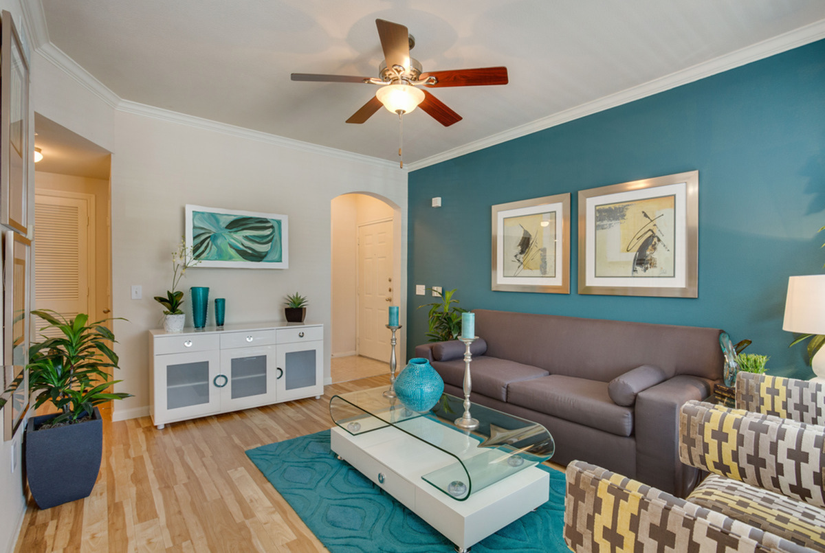 Inviting living room model at Raveneaux Apartments with teal accent wall, stylish decor, and cozy seating area for modern living.