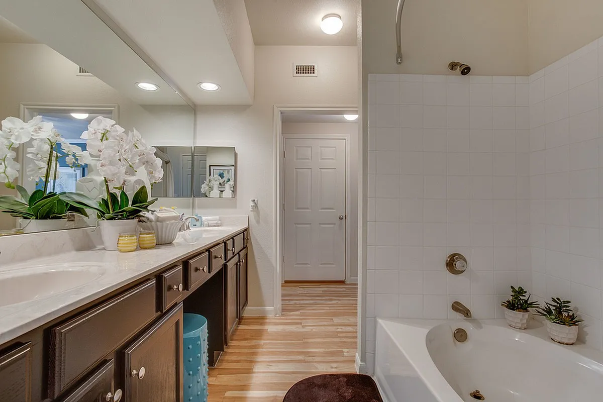 Elegant bathroom at Raveneaux Apartments in Houston, Texas featuring a sleek double vanity, luxurious soaking tub, and beautiful floral accents.