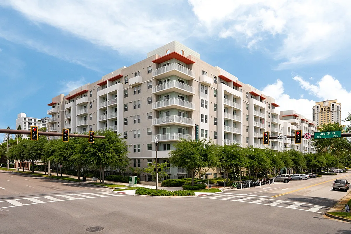Modern urban apartment building, Cottonwood Bayview, with spacious balconies and lush greenery at a bustling city intersection, under a vibrant blue sky.