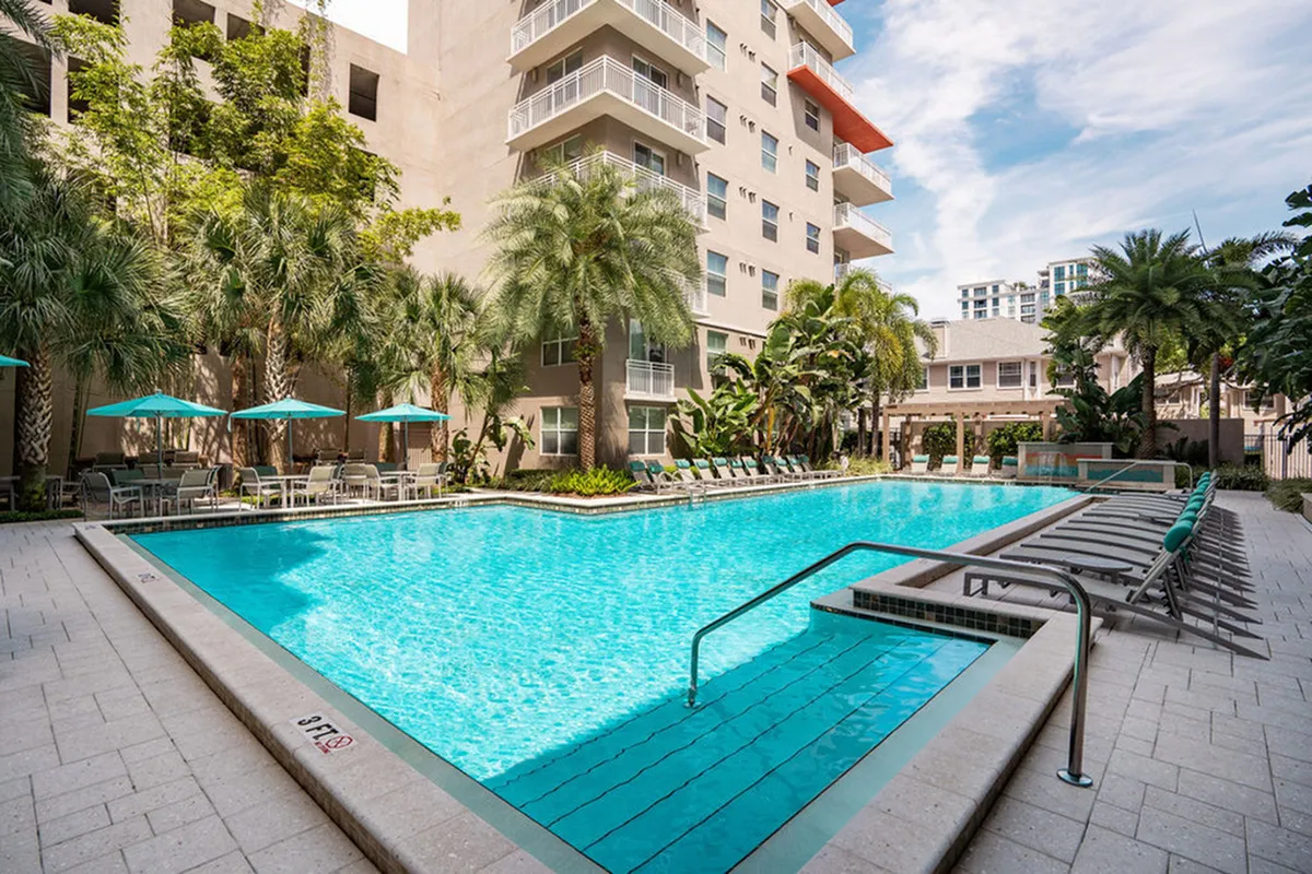 Luxurious apartment complex with a sparkling pool, surrounded by lush palm trees and elegant outdoor seating at Cottonwood Bayview Apartments.