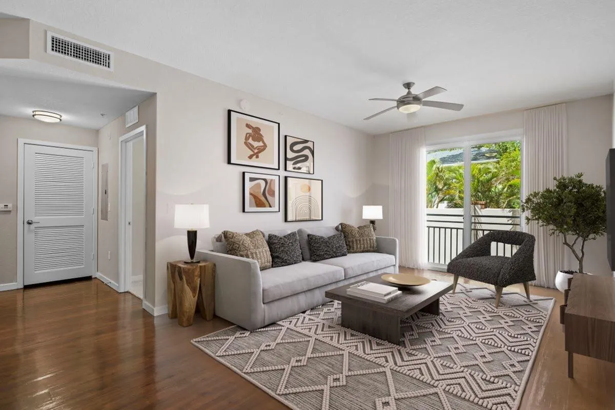 Bright and modern living room at Cottonwood Bayview with stylish decor, featuring a comfortable gray sofa, accent art pieces, elegant floor lamp, and access to a sunny balcony with lush greenery.