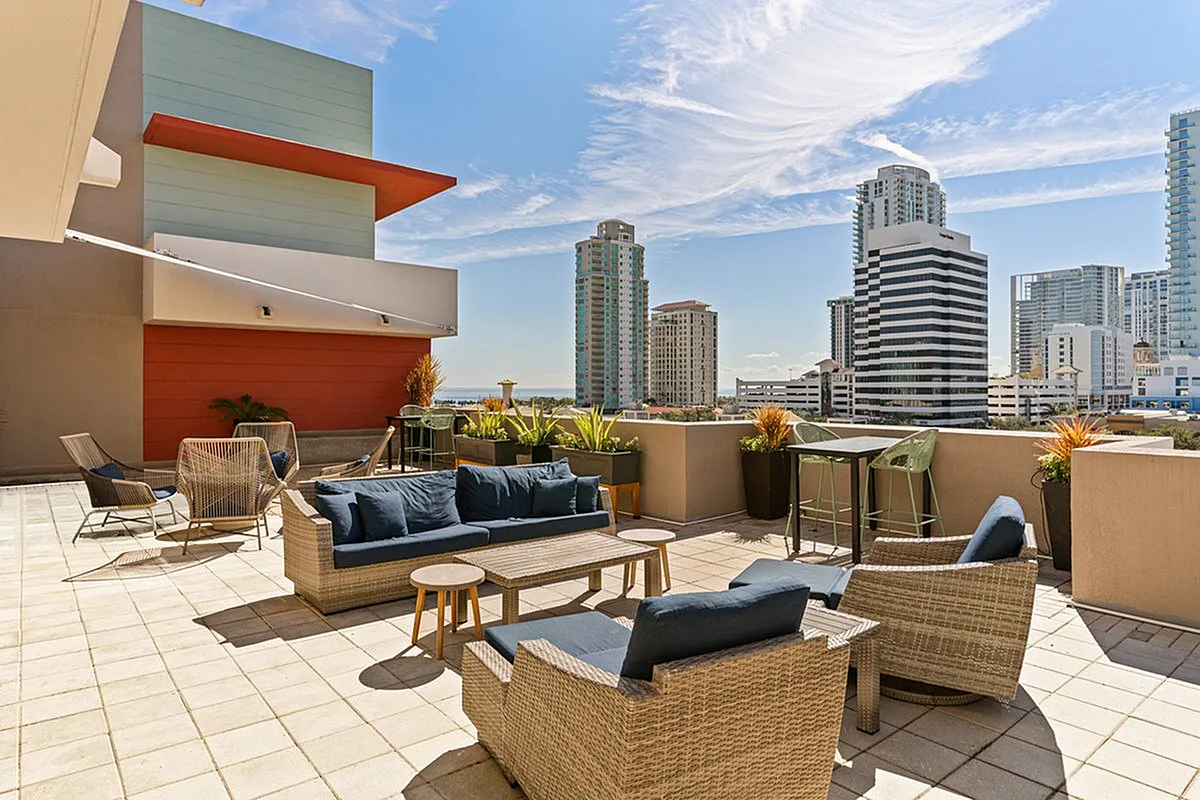 Modern rooftop terrace at Cottonwood Bayview Apartments in Downtown St. Pete with elegant wicker furniture, lush greenery, and a stunning skyline view of city skyscrapers.