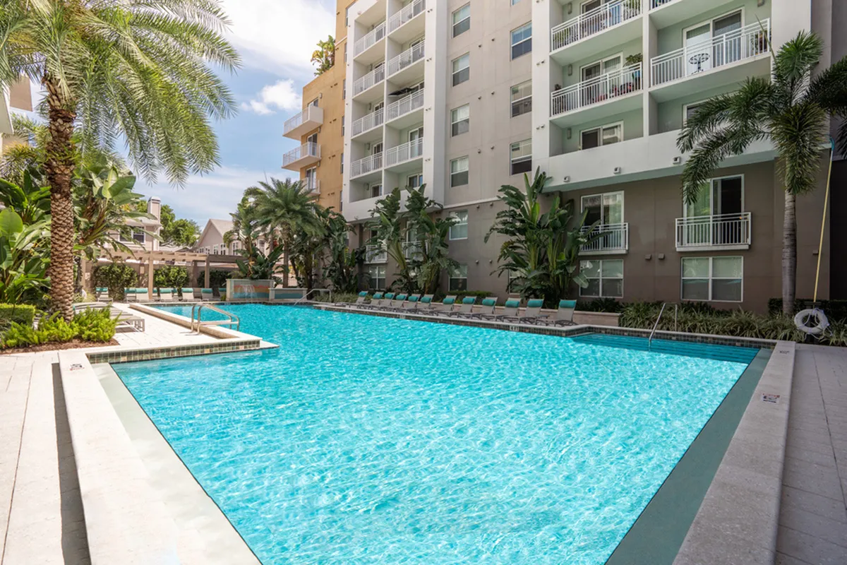 Luxurious apartment complex featuring a sparkling outdoor pool surrounded by lush palm trees and modern balconies at Cottonwood Bayview.